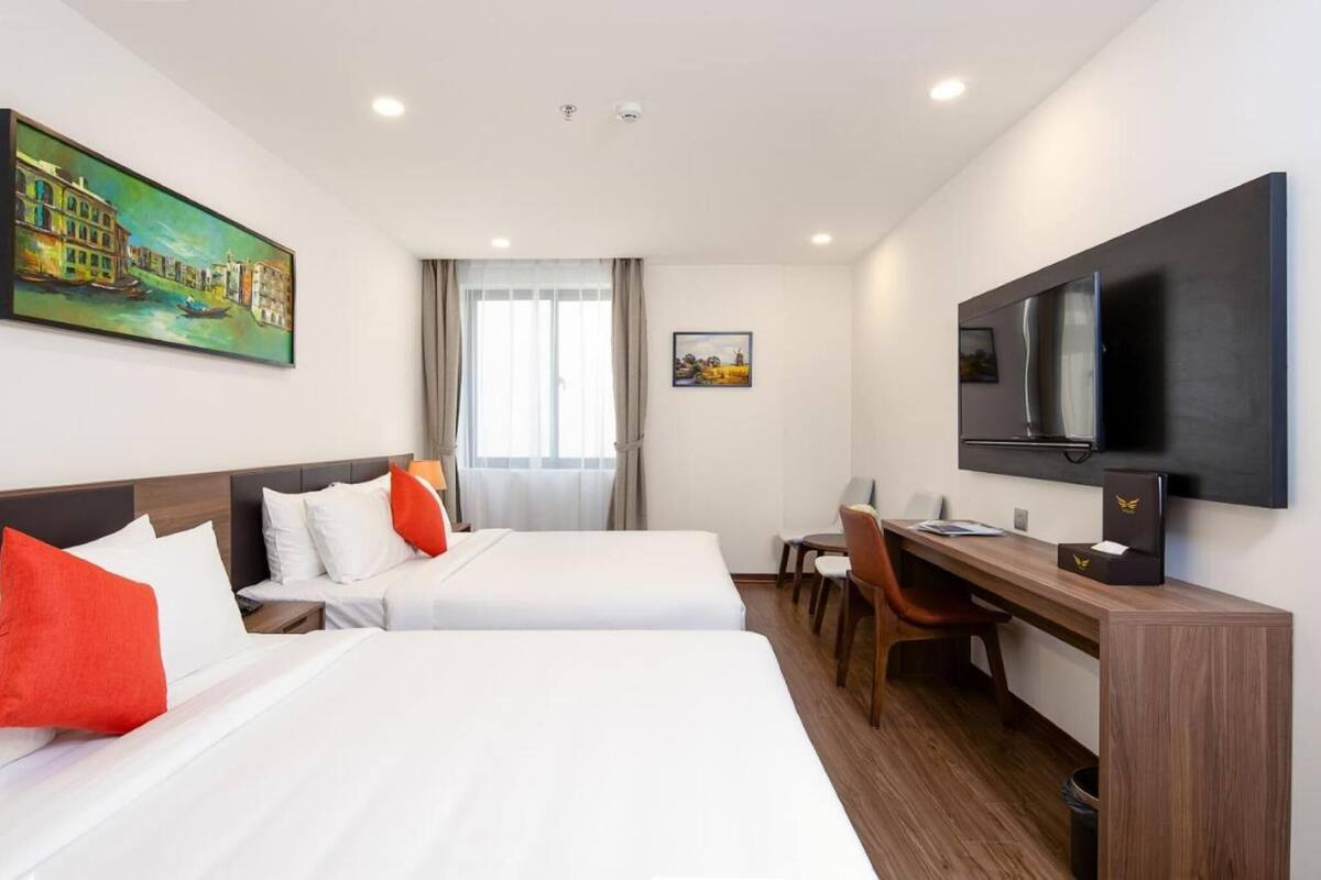Une chambre d’hôtel avec deux lits, un bureau, une chaise, une télévision et des œuvres d’art accrochées aux murs.