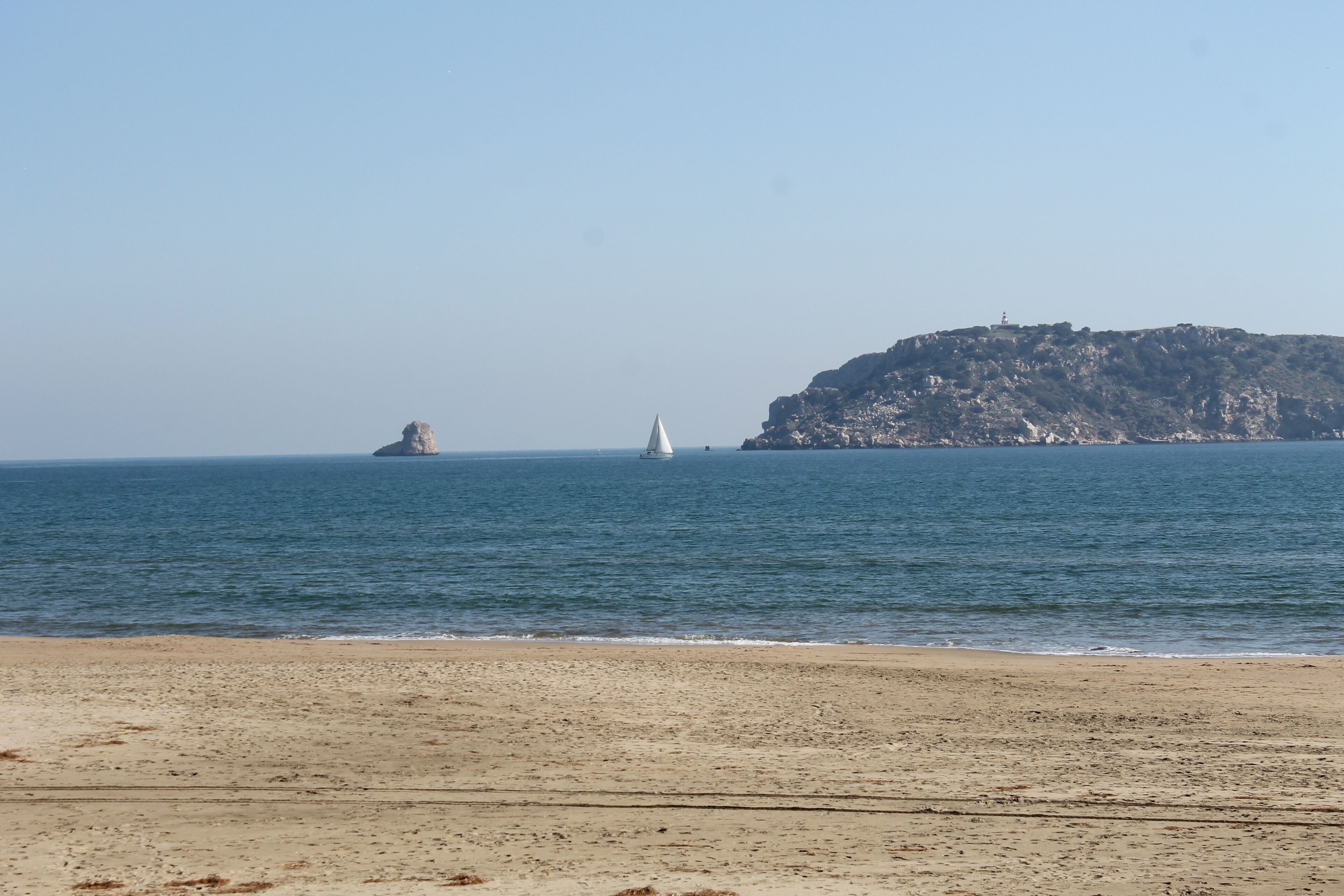Una playa con orilla arenosa, una colina rocosa al fondo y un faro.