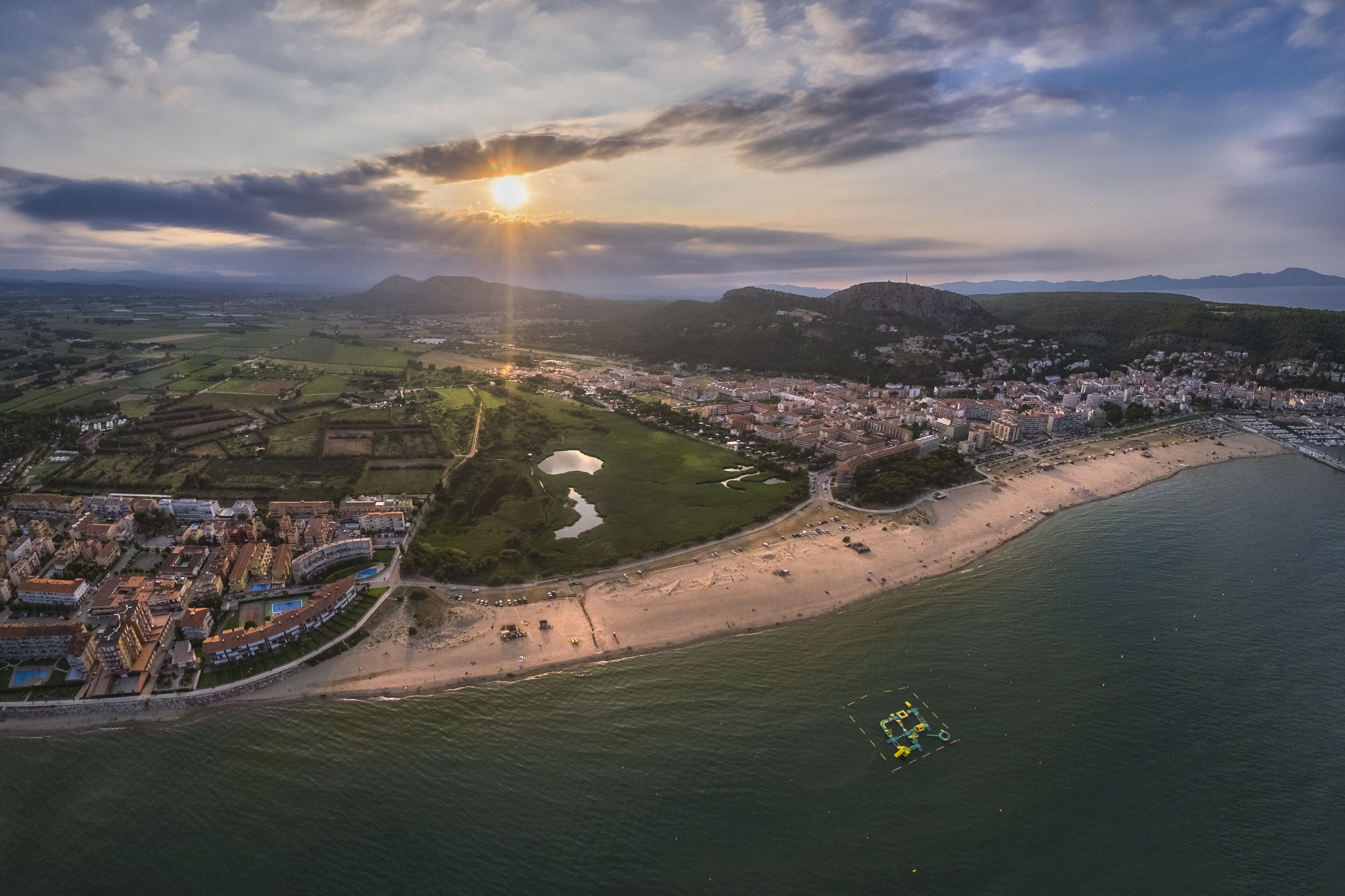 Luftaufnahme einer Küstenstadt mit Strand, einem Hafen und umliegenden Feldern.