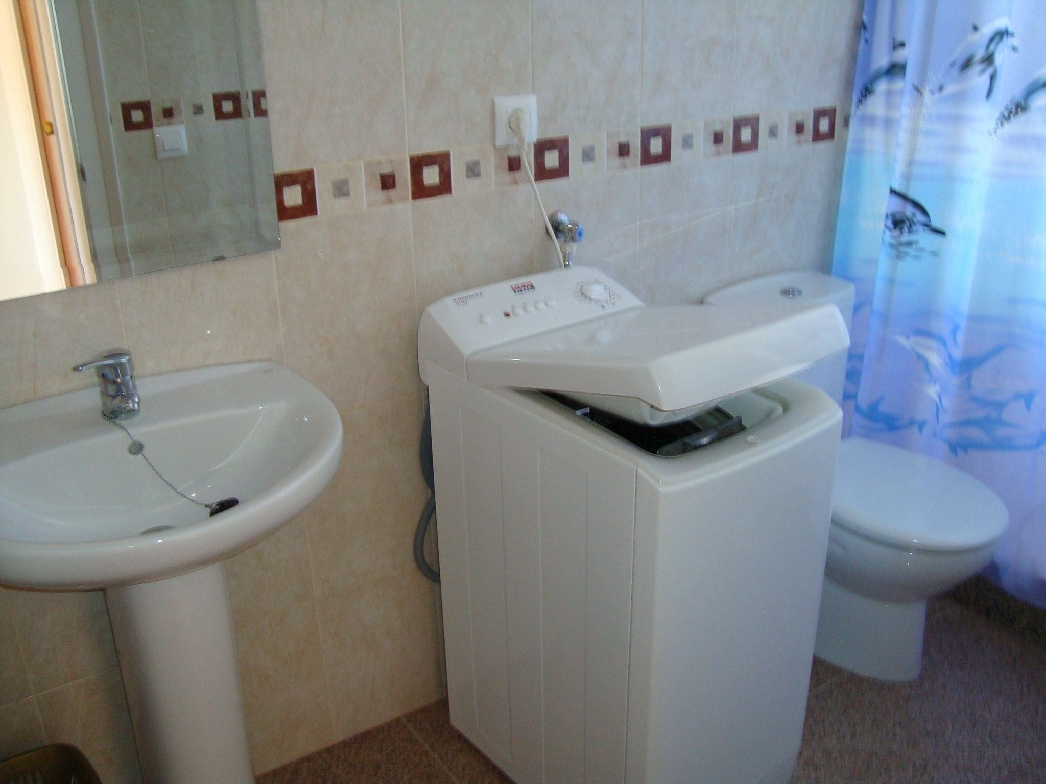 A bathroom with a sink, a washing machine, and a toilet.