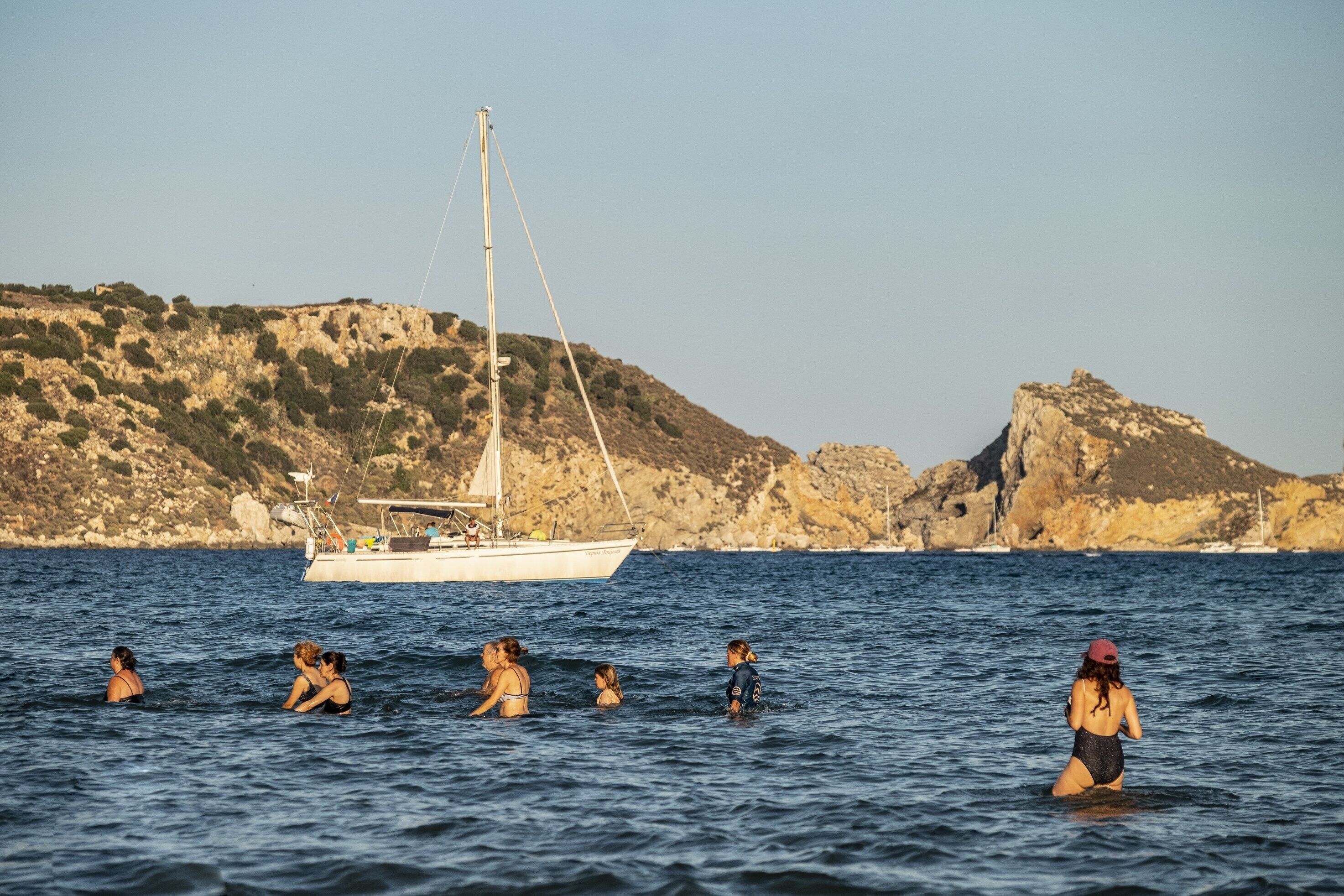 A coastal scene with a sailboat and rocky hills in the background.