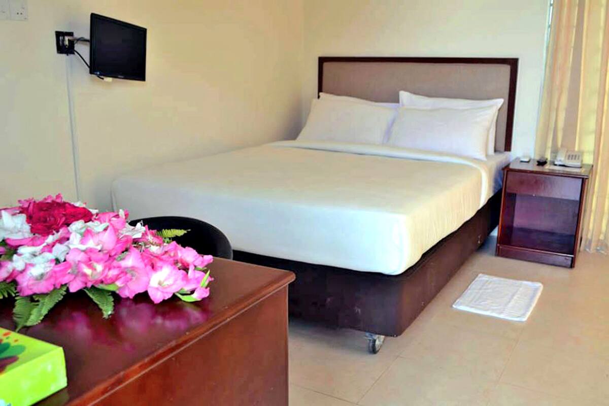 Ein Hotelzimmer mit Bett, Schreibtisch mit Blumenvase, Wandfernseher und Nachttisch mit Telefon.