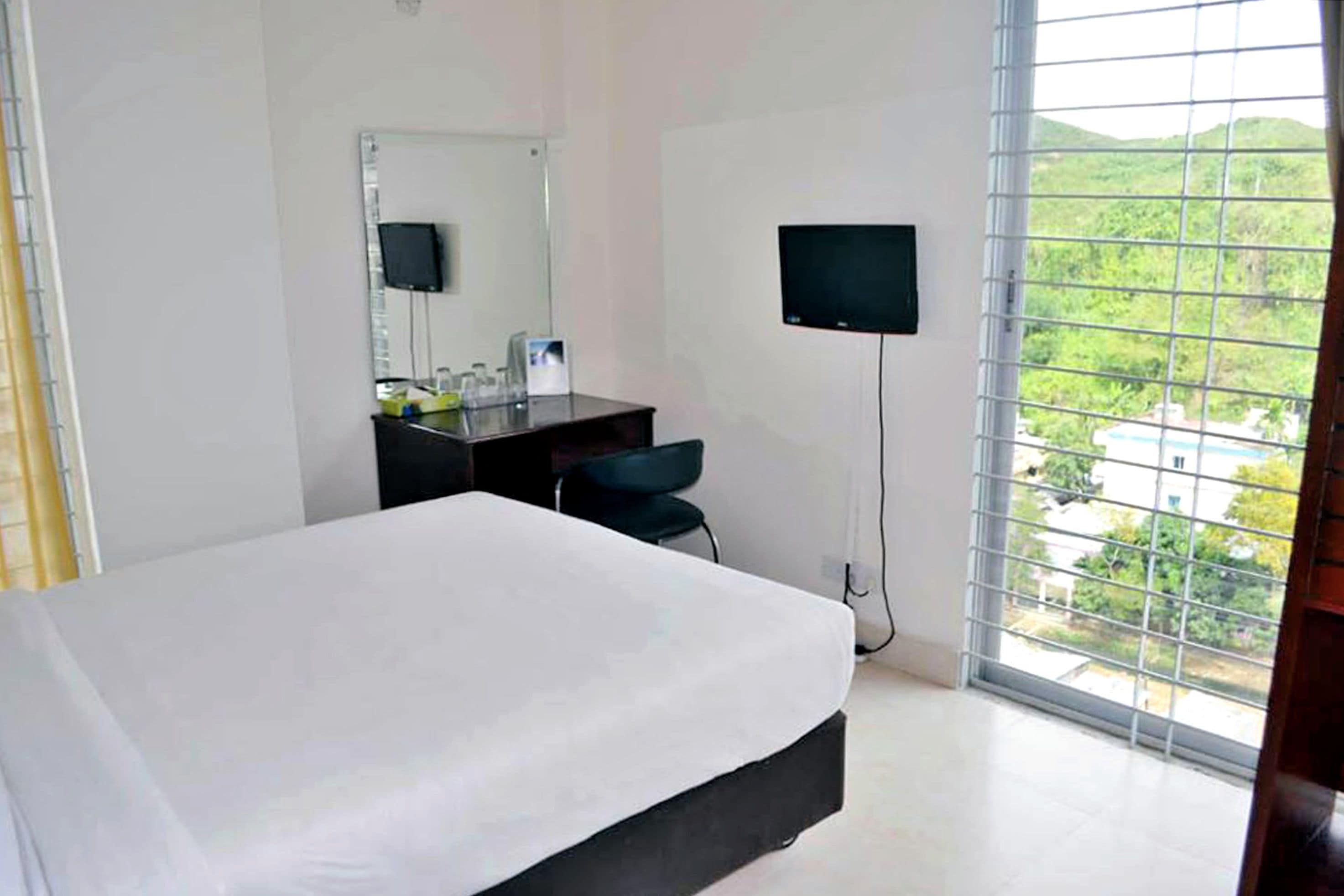 Une chambre d’hôtel équipée d’un lit, d’un bureau, d’une chaise, d’une télévision et d’une fenêtre donnant sur un paysage verdoyant.
