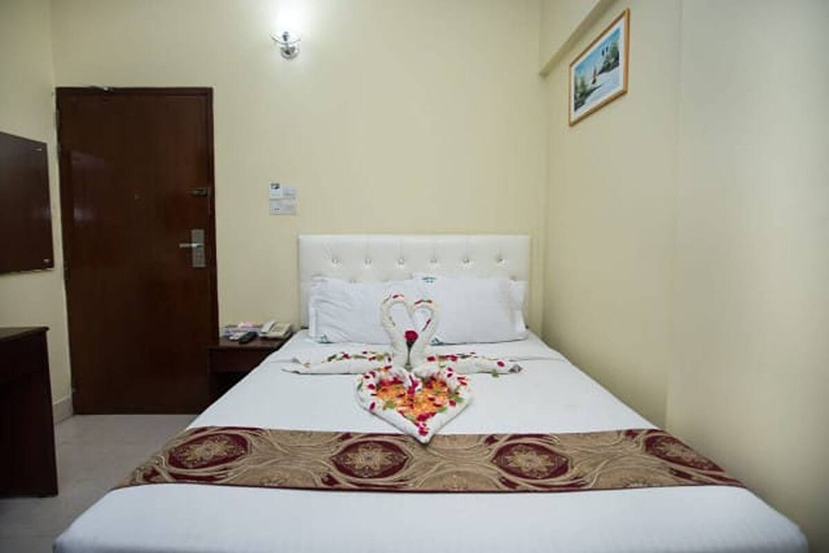 Ein Hotelzimmer mit einem aufgereihten Bett, einer Holztür, einem kleinen Tisch mit einem Telefon und einem Bild an der Wand.