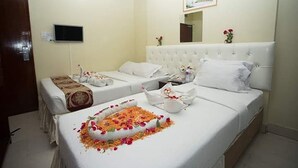 Ein Hotelzimmer mit zwei Betten, einem Fernseher, einem Spiegel und einem kleinen Tisch mit Blumen.
