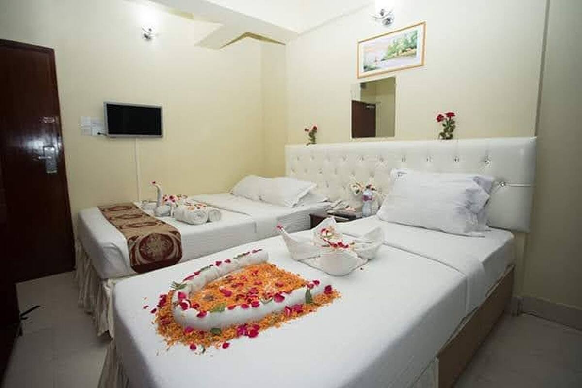 Ein Hotelzimmer mit zwei Betten, einem Fernseher, einem Spiegel und einem kleinen Tisch mit Blumen.