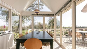 Uma área de refeições com uma mesa grande e cadeiras, janelas amplas e vista para o exterior.