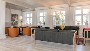 Uma sala de estar moderna com um sofá cinzento, cadeiras laranja e teto de madeira.