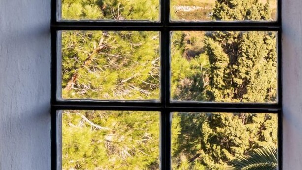 Une fenêtre donnant sur un paysage montagneux, avec des arbres et un bâtiment.
