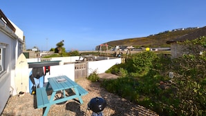 Een terras met een tafel, een barbecue en surfplanken die tegen een muur leunen.
