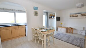 Een eetruimte met een houten tafel en stoelen, een keuken met houten keukenkastjes en een groot raam.