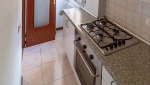 A narrow kitchen with a gas stove, a wooden door, and a window with blinds. - Bologna Fiera Guest House (Bologna)