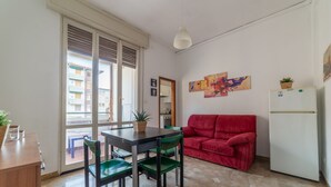 A compact living space with a dining table, green chairs, a red sofa, a white refrigerator, and a potted plant. - Bologna Fiera Guest House (Bologna)