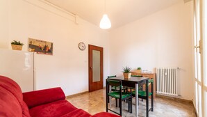 A compact living space with a red sofa, a dining table with chairs, a small kitchen area, and a radiator. - Bologna Fiera Guest House (Bologna)