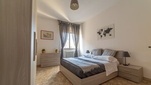 A bedroom with a bed, bedside tables, a dresser, a window with curtains, a world map on the wall, and a potted plant. - Bologna Fiera Guest House (Bologna)