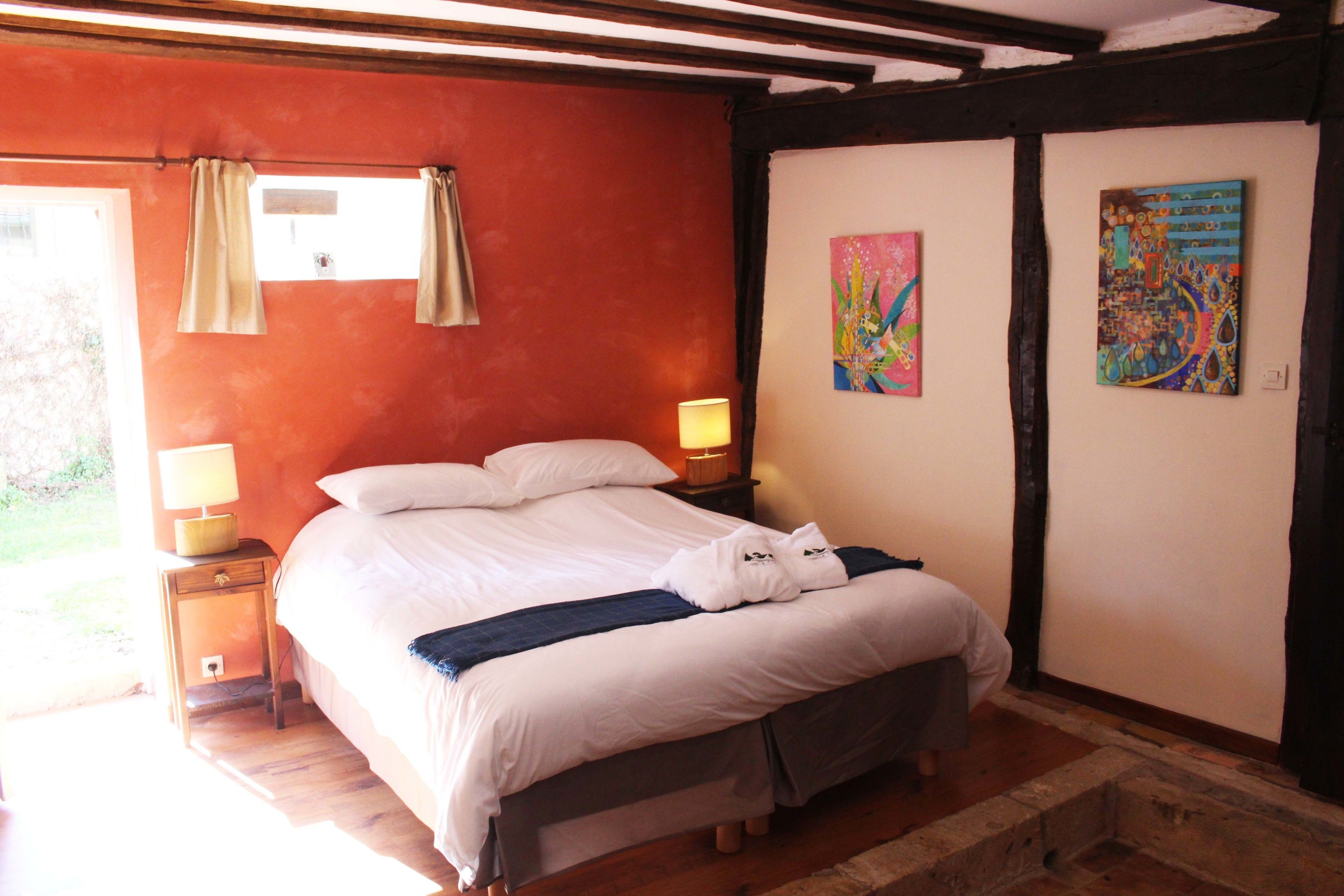 A bedroom with a bed, two bedside lamps, and two paintings on the wall.