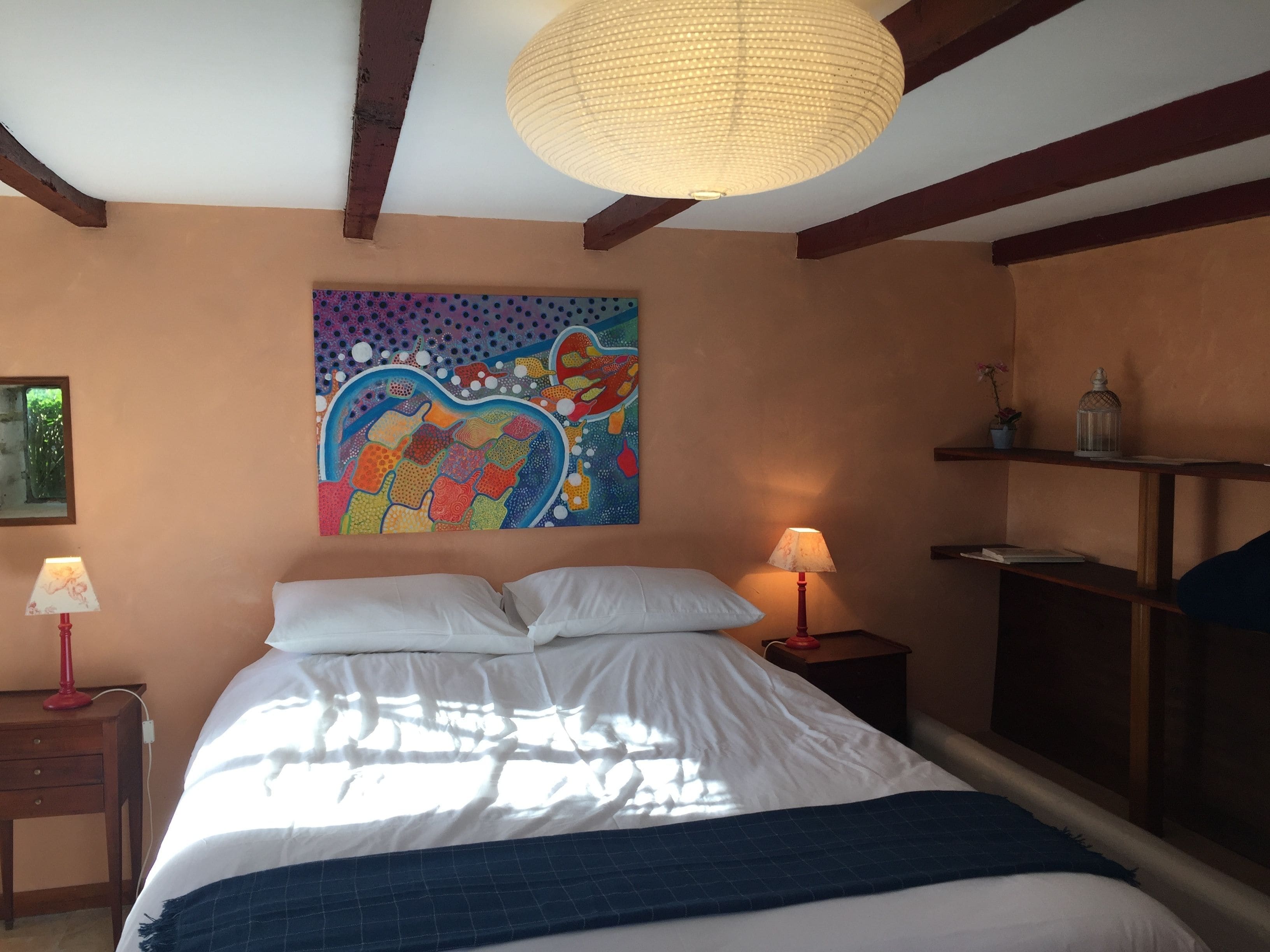 Un dormitorio con cama, dos mesitas de noche, una obra de arte en la pared y una lámpara colgante.