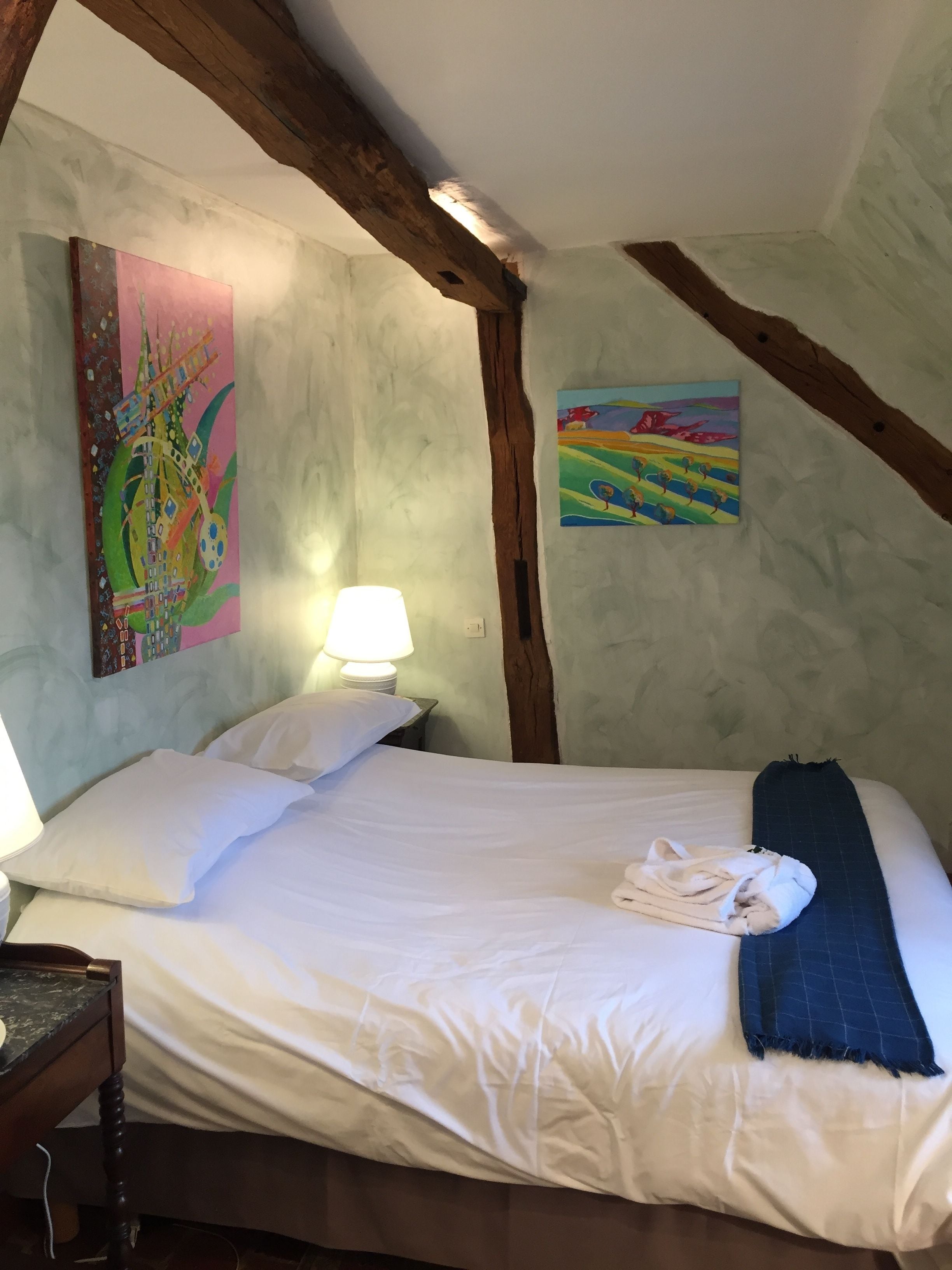 Un dormitorio con cama, almohadas, lámpara, un cuadro y estructura de vigas de madera.