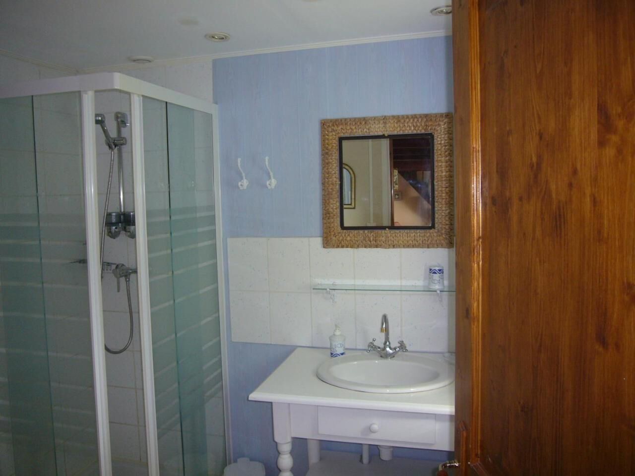Un baño con cabina de ducha de vidrio, lavabo blanco y espejo con marco decorativo.