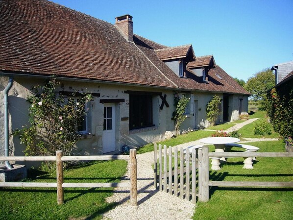 A traditional house with a sloped roof, a wooden fence, and a gravel pathway leading to the entrance.
