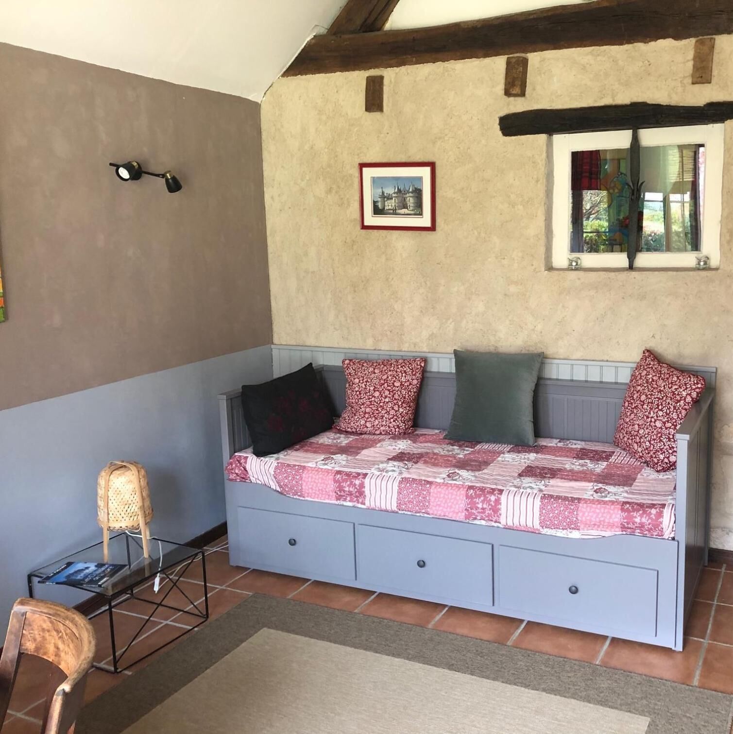 A bedroom with a bed, a chair, a small table, and a picture on the wall.