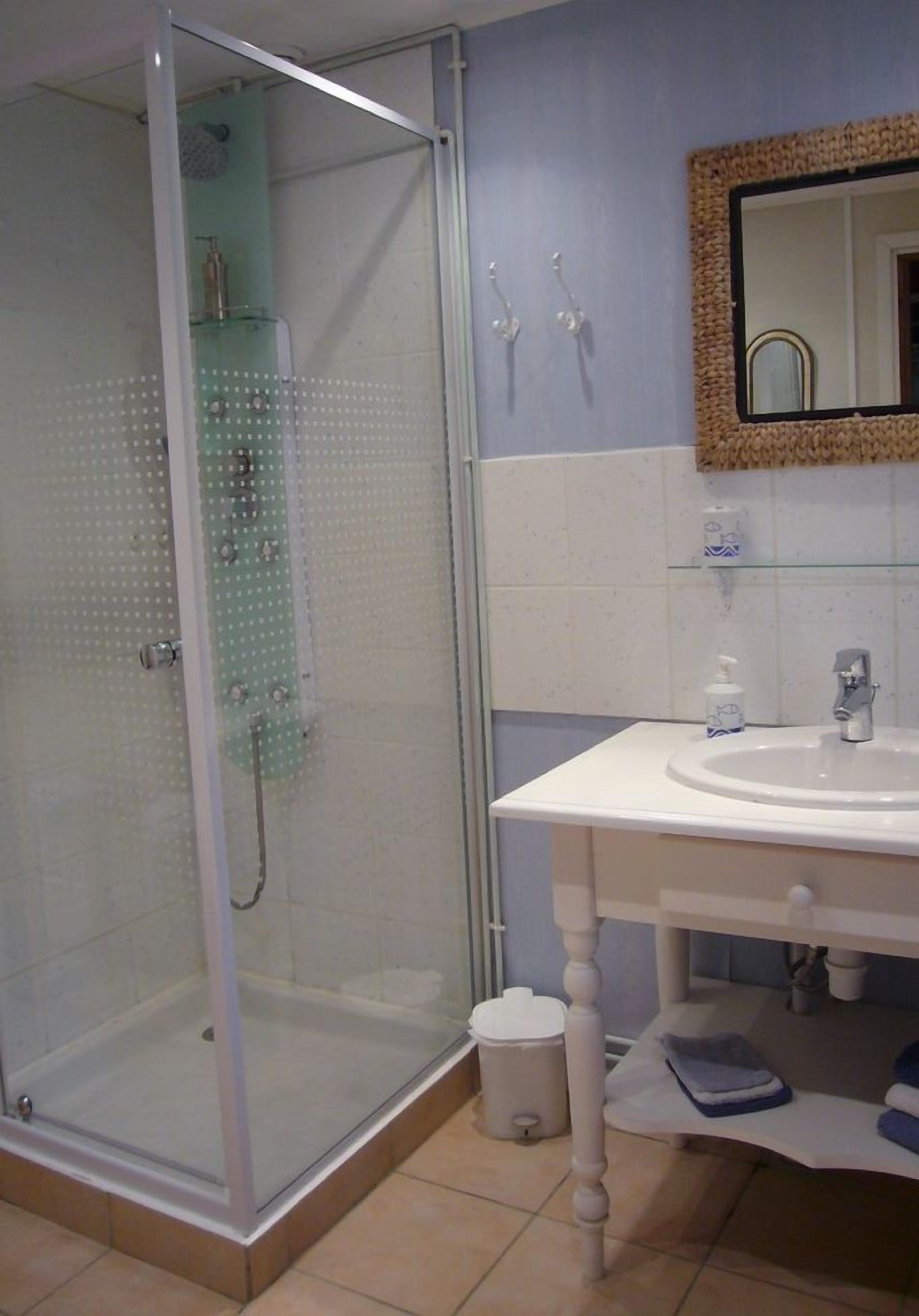 Une salle de bain avec une douche à parois de verre, un lavabo blanc et un miroir doté d’un cadre tressé.