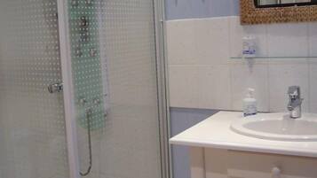 Une salle de bain avec une douche à parois de verre, un lavabo blanc et un miroir doté d’un cadre tressé.