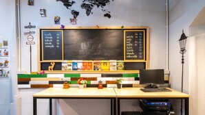 A small, modern workspace with a chalkboard menu listing prices, a world map, and various travel-themed decorations. - Sip N' Camp - Hostel (Bangkok)