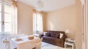 A well-lit living room with a dining area, a brown sofa, and a small table with a lamp.