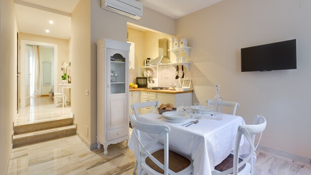 A dining area with a white table, chairs, and a TV mounted on the wall.
