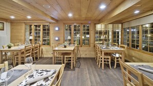 Un intérieur en bois avec de nombreuses tables et chaises, de grandes fenêtres et des luminaires au plafond.
