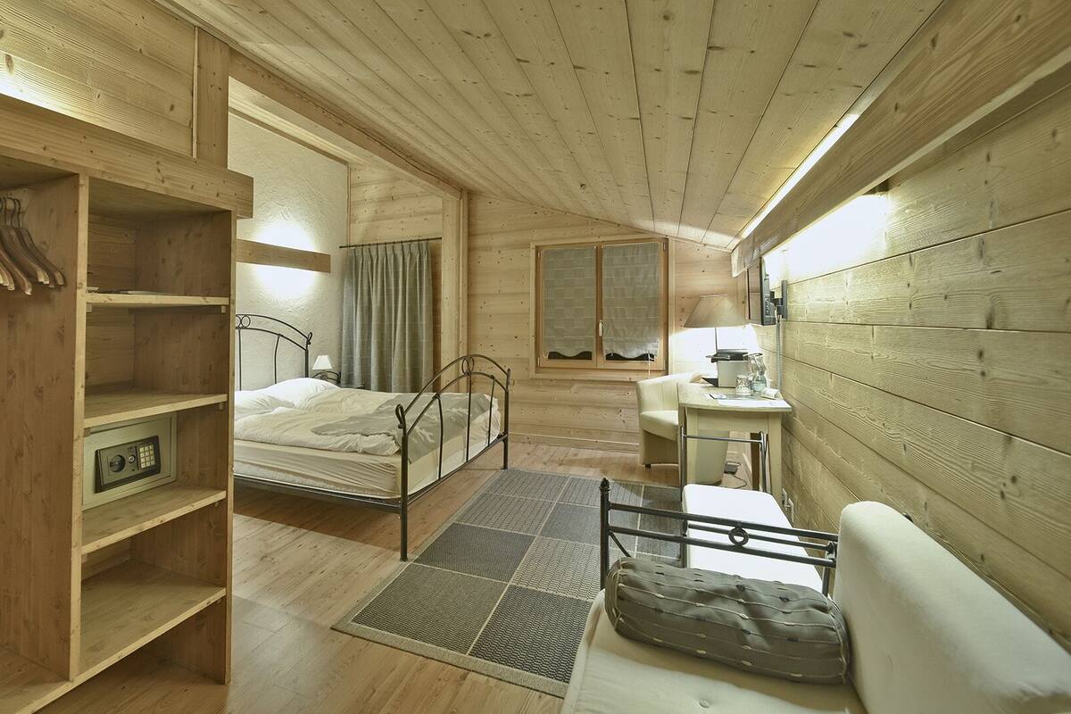 Une petite pièce de cabane en bois comprenant un lit, un petit bureau, un miroir et une armoire.