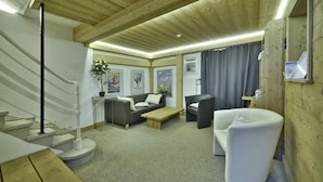 Une pièce chaleureuse avec un plafond en bois, un canapé, un fauteuil, une table basse et un escalier.
