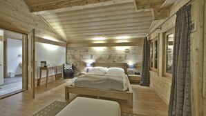 Une chambre dans un chalet en bois, avec un lit, des tables de chevet, une chaise et une fenêtre avec des rideaux.