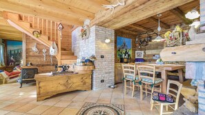 A rustic cabin interior with a wooden stove, a dining table with chairs, a brick fireplace, and a staircase with wooden railings. - Lovely home in Lamon(BL) with WiFi (Lamon(BL))