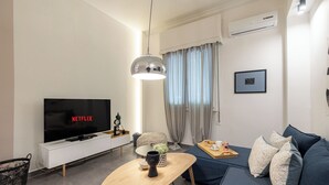 A modern living room with a flat-screen TV, a wooden coffee table, a blue sofa, and a small side table with a tray of snacks. - Cosy apt near Piraeus central port, Mikrolimano port & Pasalimani port. (Pireas)