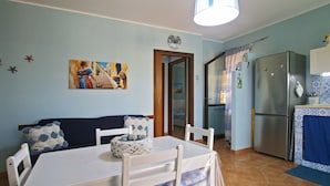 A compact kitchen with a refrigerator, a dining table with chairs, and a painting on the wall.