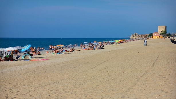 A wide sandy beach with umbrellas and people.