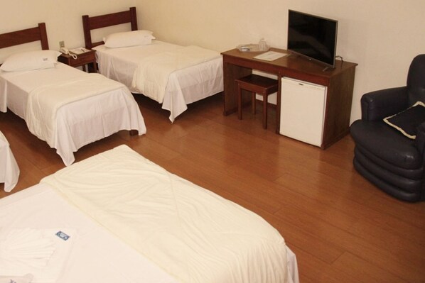 Habitación de hotel con dos camas individuales, un escritorio con televisor, un refrigerador pequeño y una silla negra.