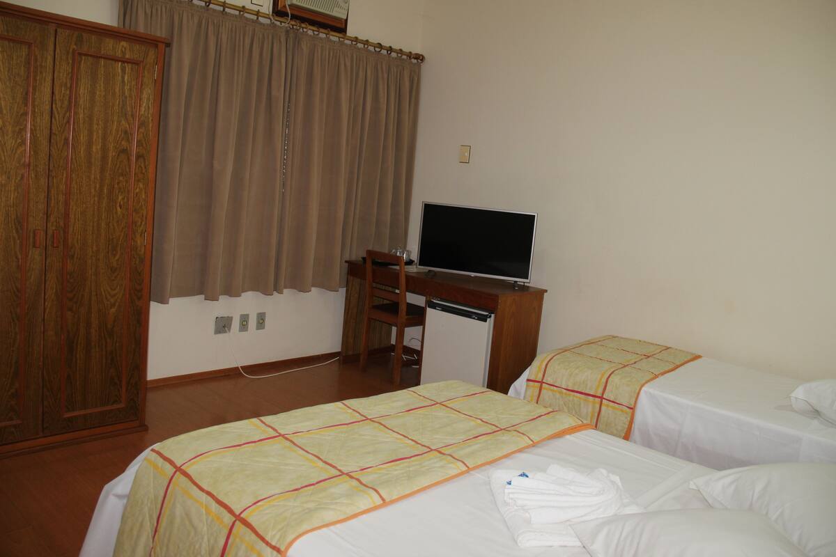 A hotel room with two beds, a desk with a television, and a wardrobe.