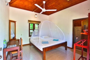 Un dormitorio con techo de madera, una cama con mosquitero, una silla, una mesa y una ventana.