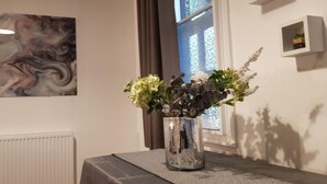 Ett rum med ett bord som har ett mönster som liknar marmor, en vas med blommor, ett element och ett fönster med gardiner.