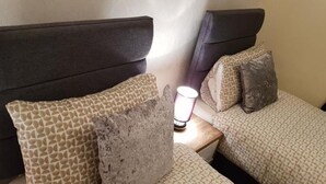 Ett hotellrum med två sängar, var och en med ett mönstrat sängöverkast och en sänggavel. Ett nattduksbord med en lampa står synligt mellan sängarna.