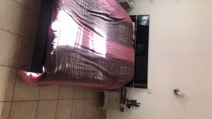 A room with a bed covered in a purple blanket, a window, a small cabinet, and a wall-mounted light fixture. - Grand t 2 on Bastia (Bastia)