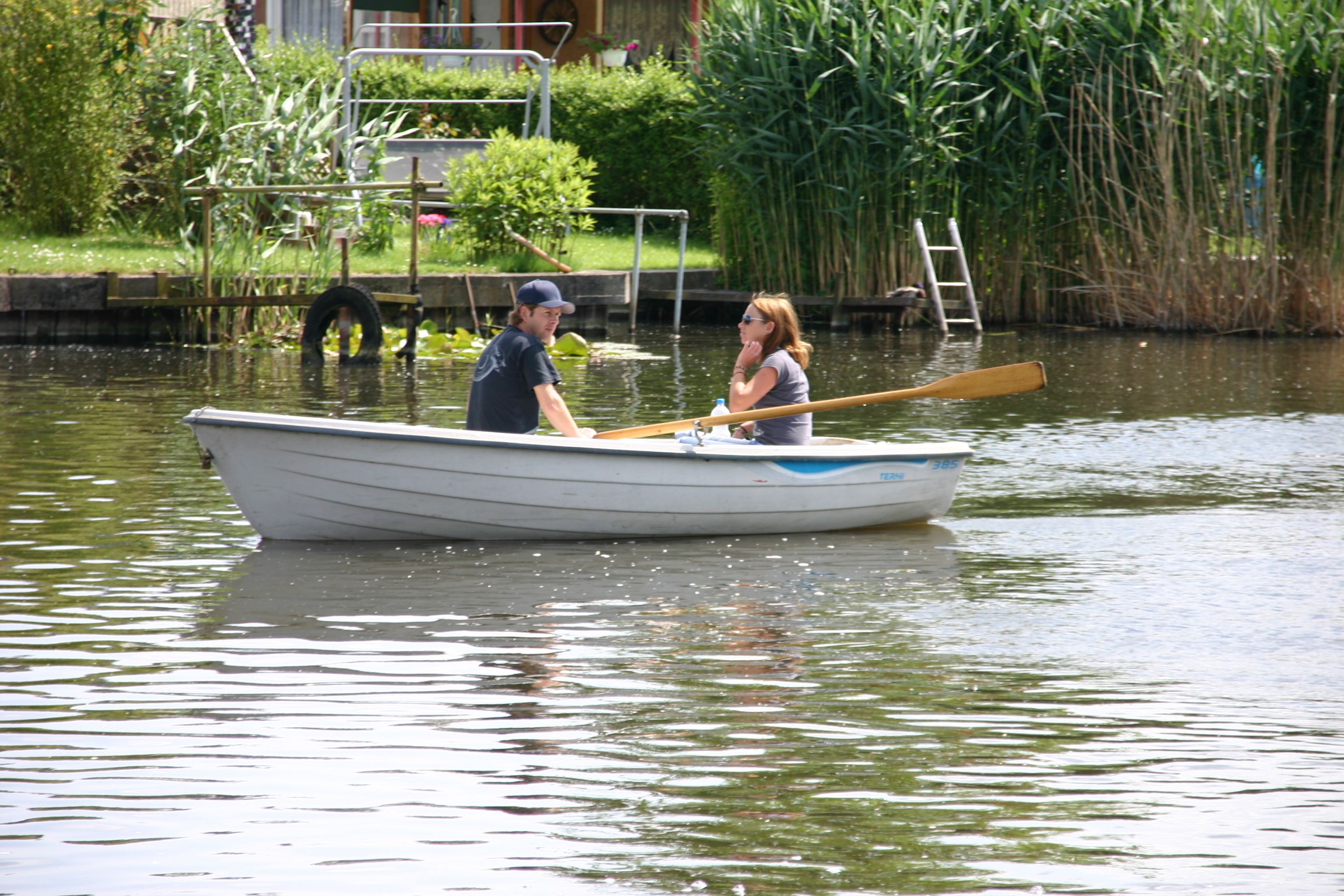 A small rowboat on calm water with two people, one paddling.