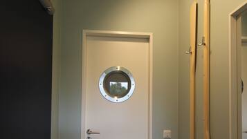 A hallway with a white door, wooden flooring, and a round mirror on the door.