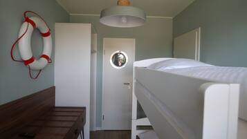 Cozy bedroom with a bunk bed arrangement, featuring a round mirror, life preserver, and simple seating area.