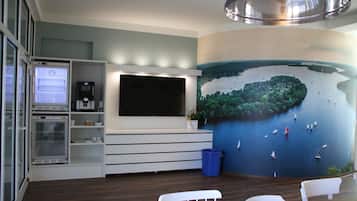 Una habitación moderna con una televisión de pantalla plana grande montada en un mueble blanco, un mural de un lago con barcos y una lámpara de techo.