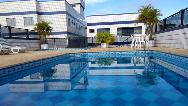 A swimming pool with a tiled edge and a view of a building with a tiled facade and windows. - Js Palace Hotel (Alfenas)