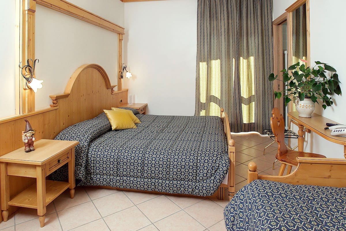 Quarto com cama de madeira, mesa de cabeceira, cômoda, espelho e planta em vaso.